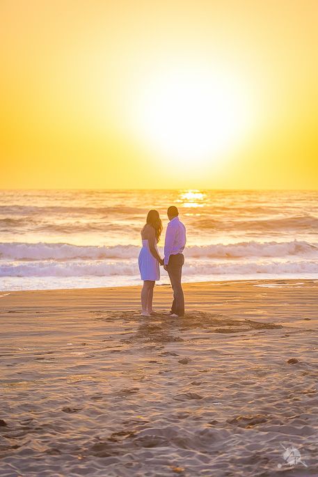 Silhouetted couple standing on beach during dramatic golden sunset.