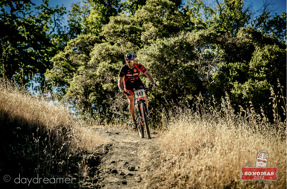Scenic mountain biking trail winding through dry grass and oak trees.