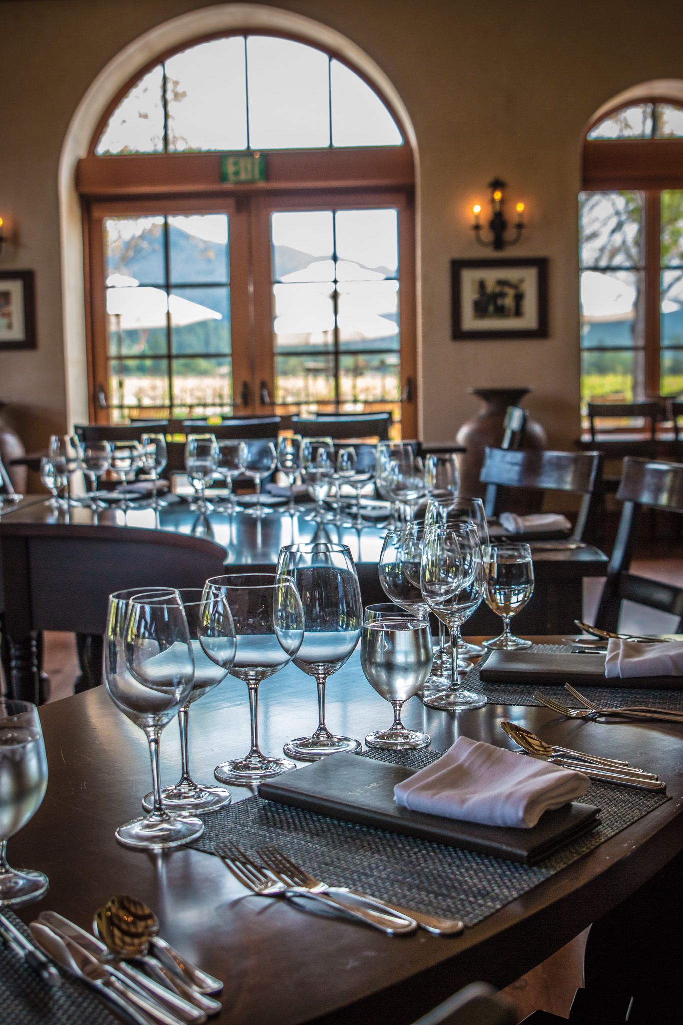 Formal dining room setup with wine glasses and place settings beneath arched windows.