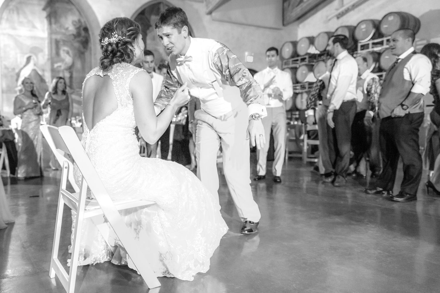 A black and white photo captures a couple during a lively first dance at their wedding reception.