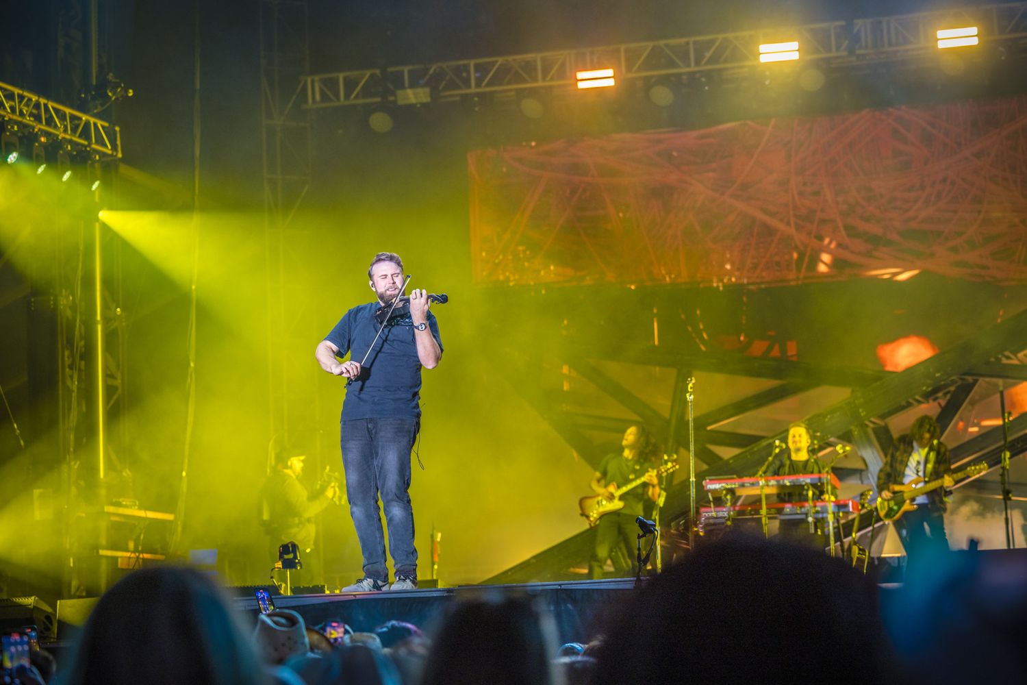 A performer stands on stage illuminated by bright yellow-green stage lighting during a concert.