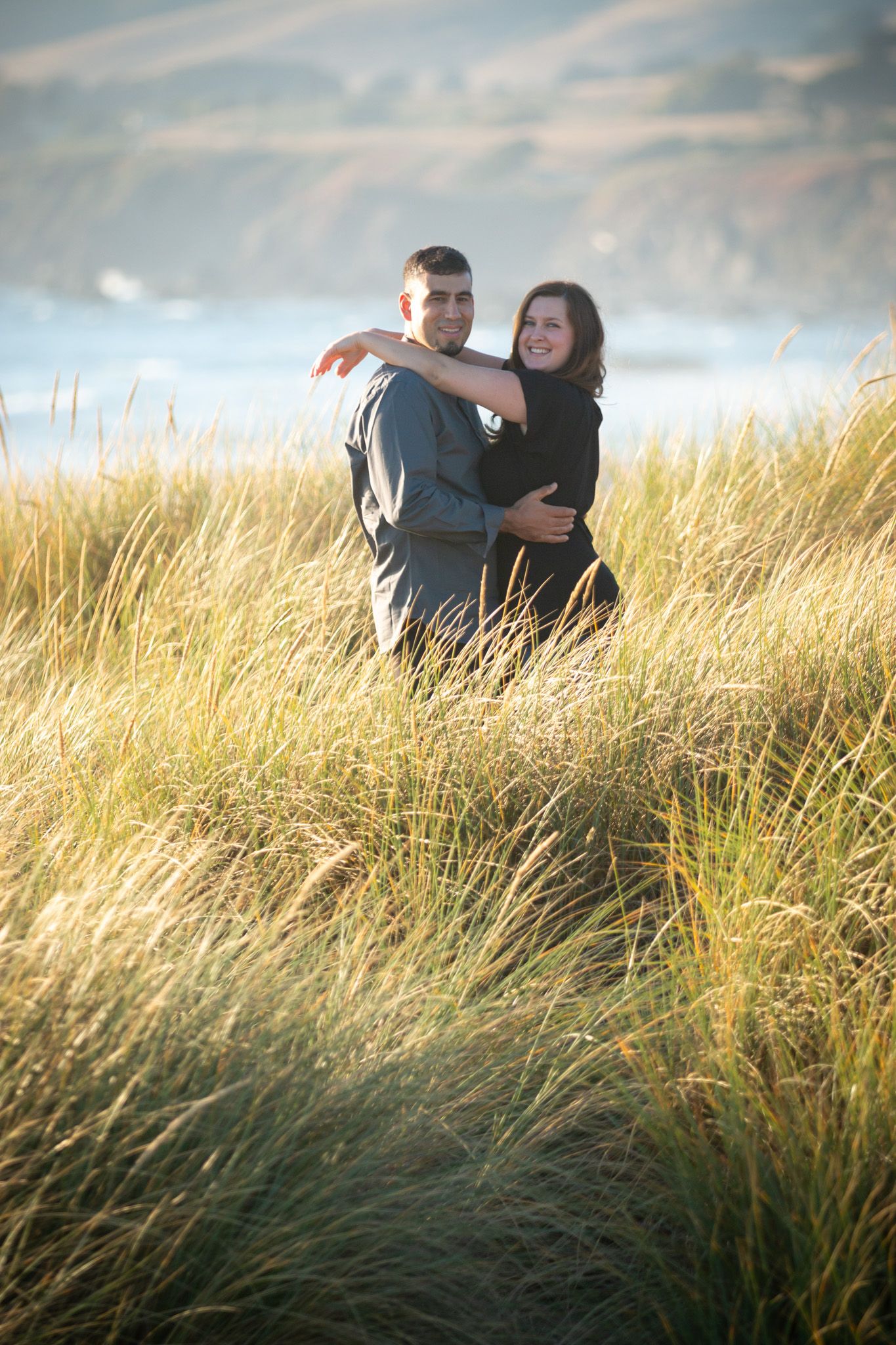 Happy couple sharing an intimate moment among tall grass near the ocean.