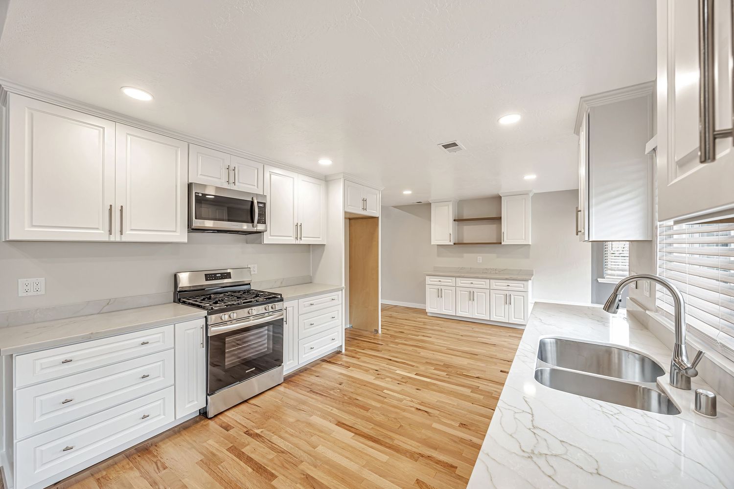 Modern kitchen renovation with white cabinetry, gas range, and built-in microwave.