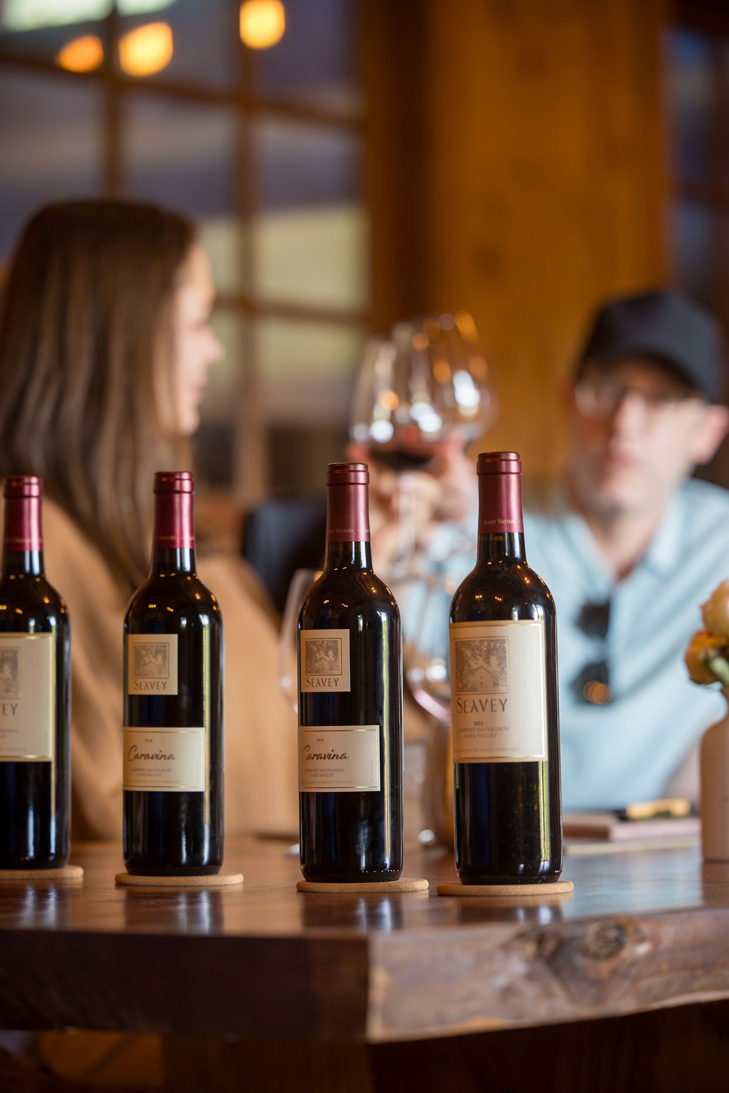 Wine bottles lined up for tasting on a wooden counter with warm lighting in the background.