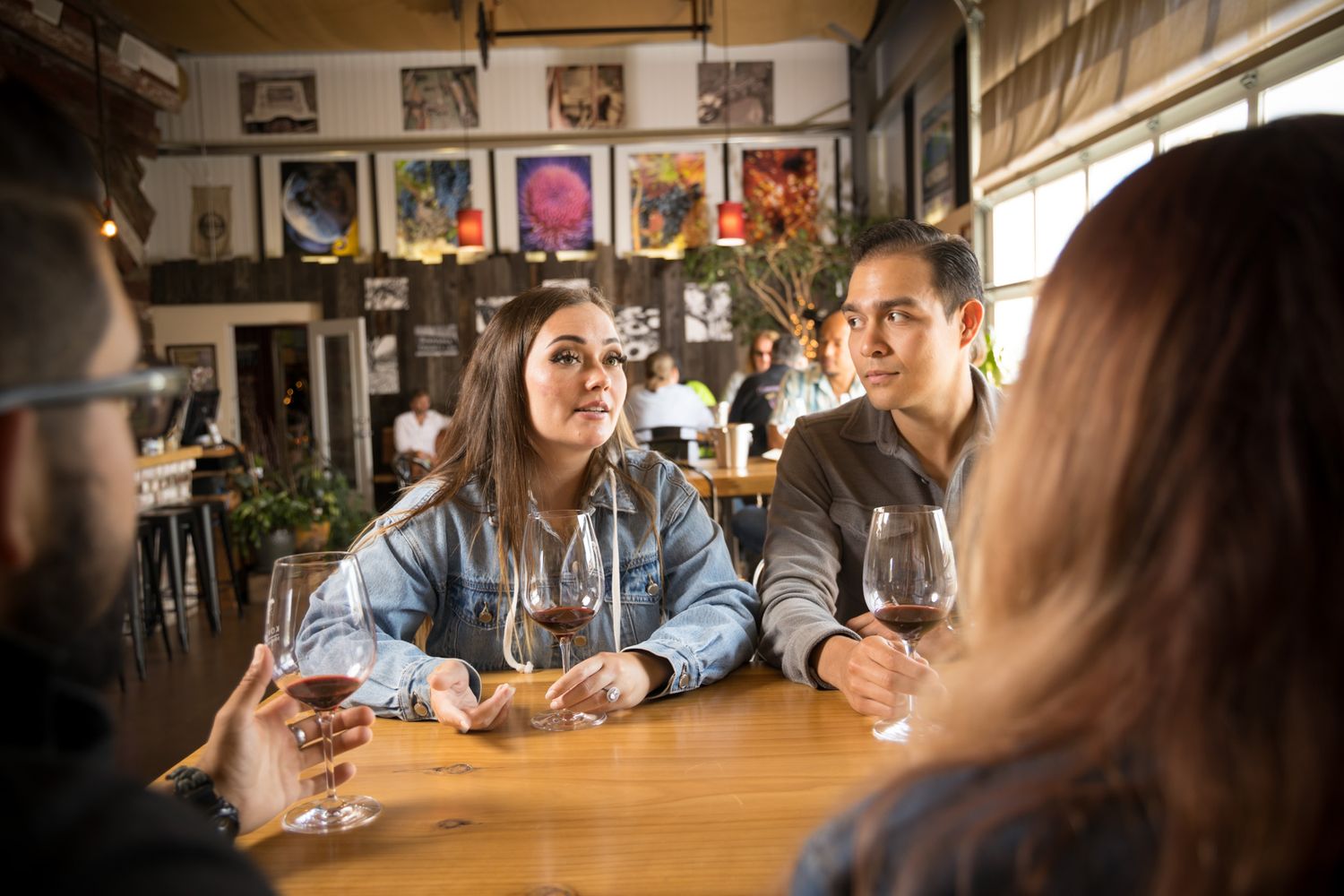 Friends enjoying wine and conversation at a rustic bar with framed artwork on the walls.