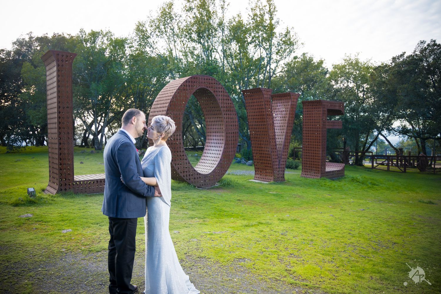 Five photos showing a couple in formal attire embracing in front of decorative outdoor sculptures and greenery.