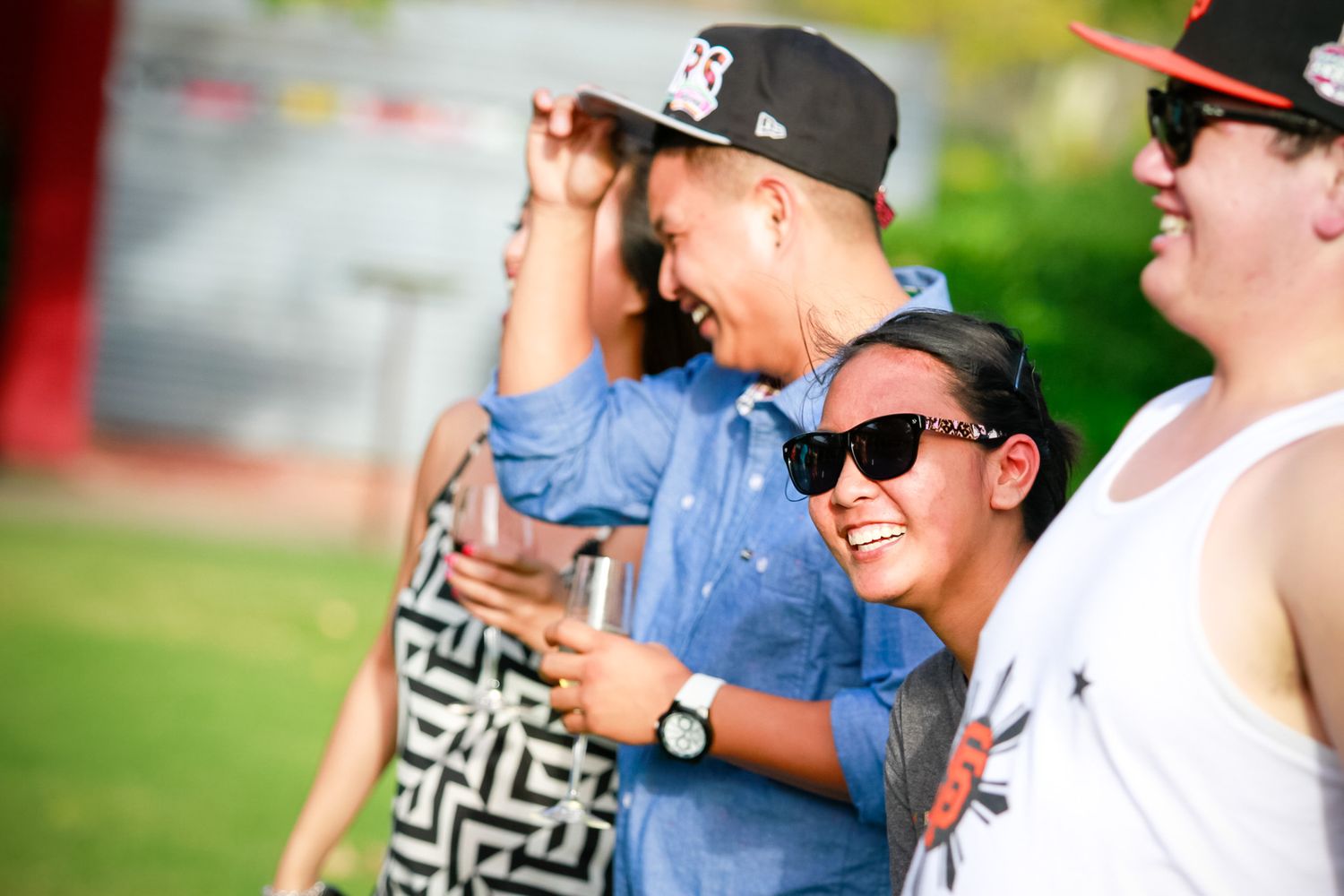 Friends laughing and having fun at an outdoor gathering wearing casual attire and sunglasses.