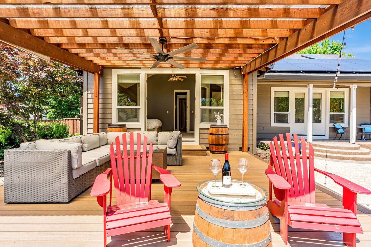 Covered patio space with red Adirondack chairs and gray sofa under wooden pergola.