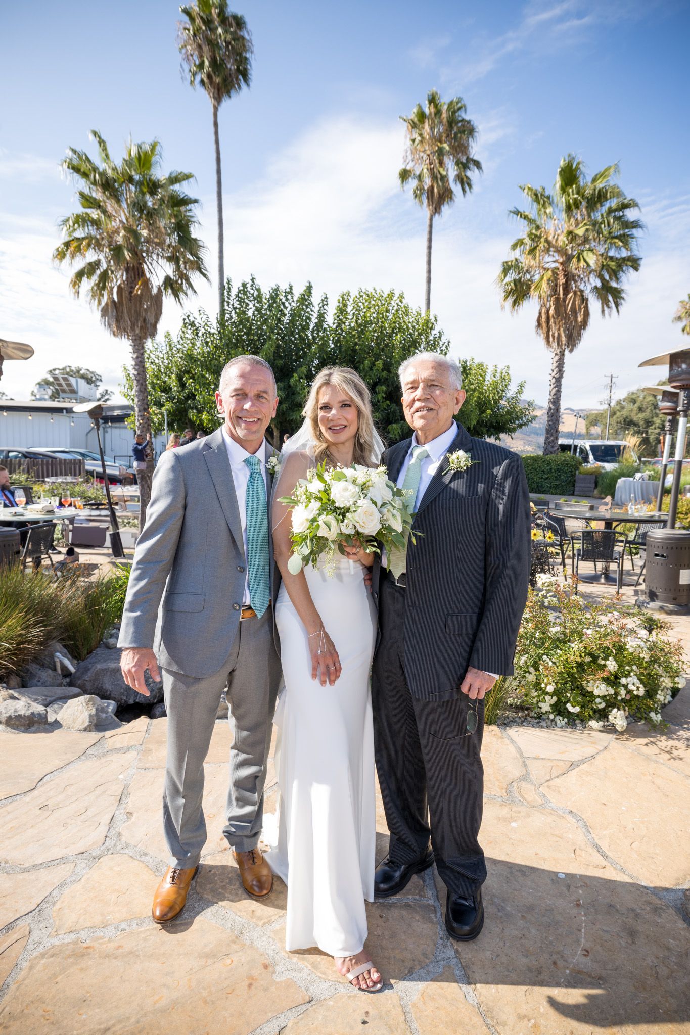 Outdoor wedding portrait with tall palm trees and stone patio background.