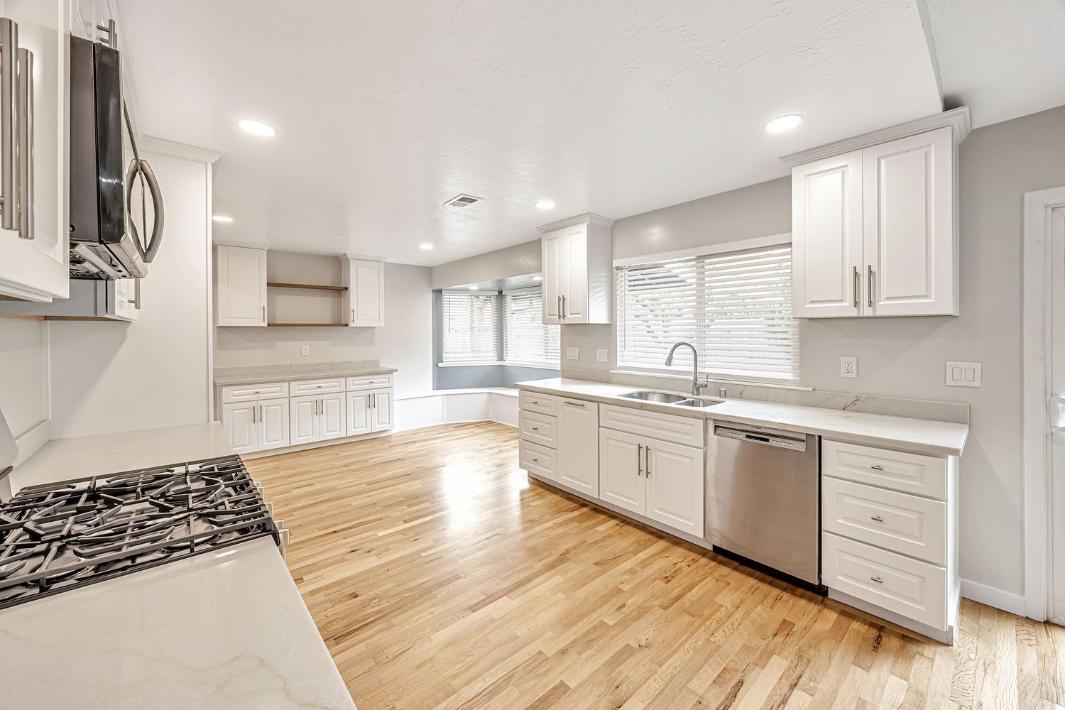 L-shaped kitchen with white shaker cabinets, stainless appliances, and light wood flooring.