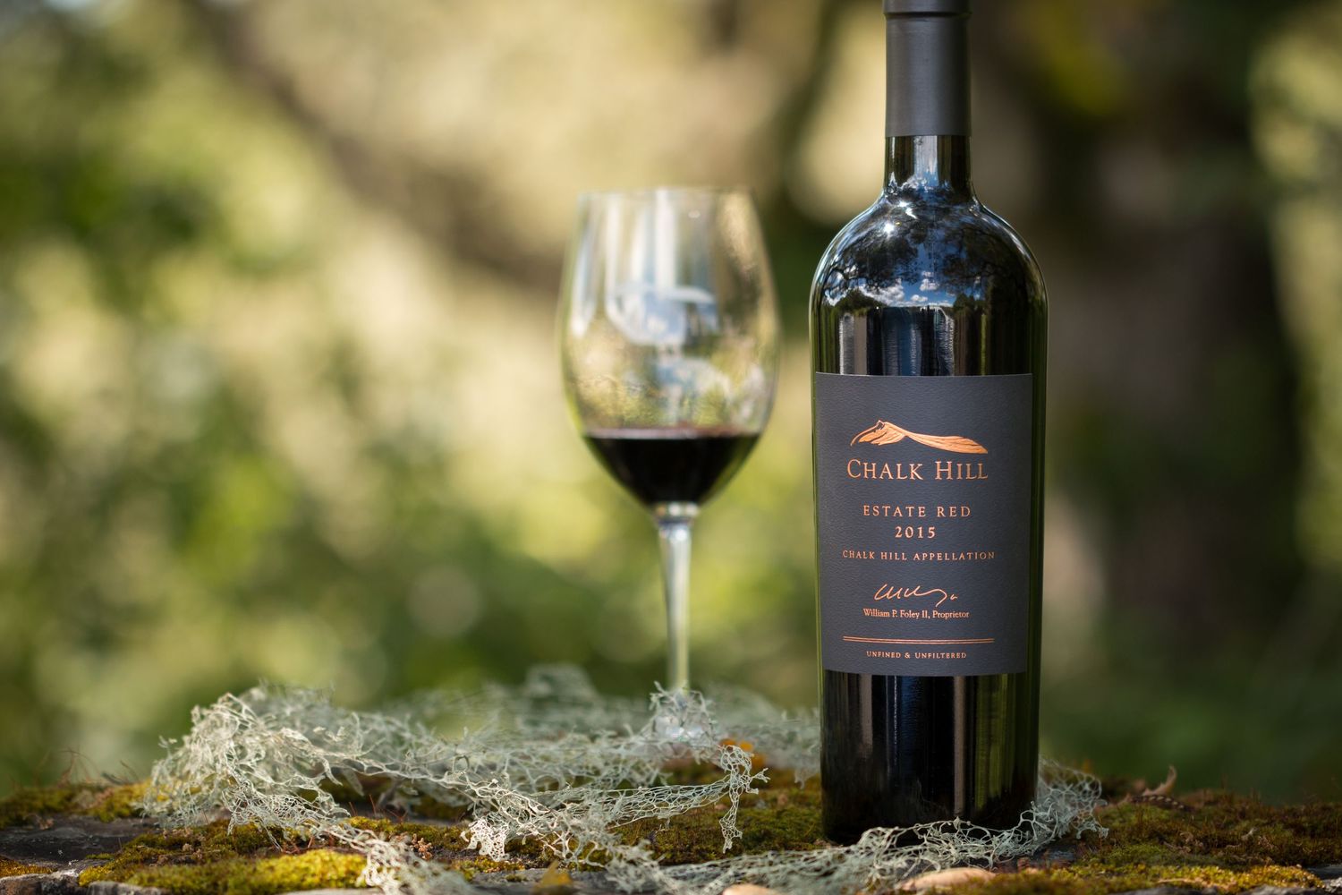 Chalk Hill wine bottle and glass staged on mossy rock with natural bokeh background.