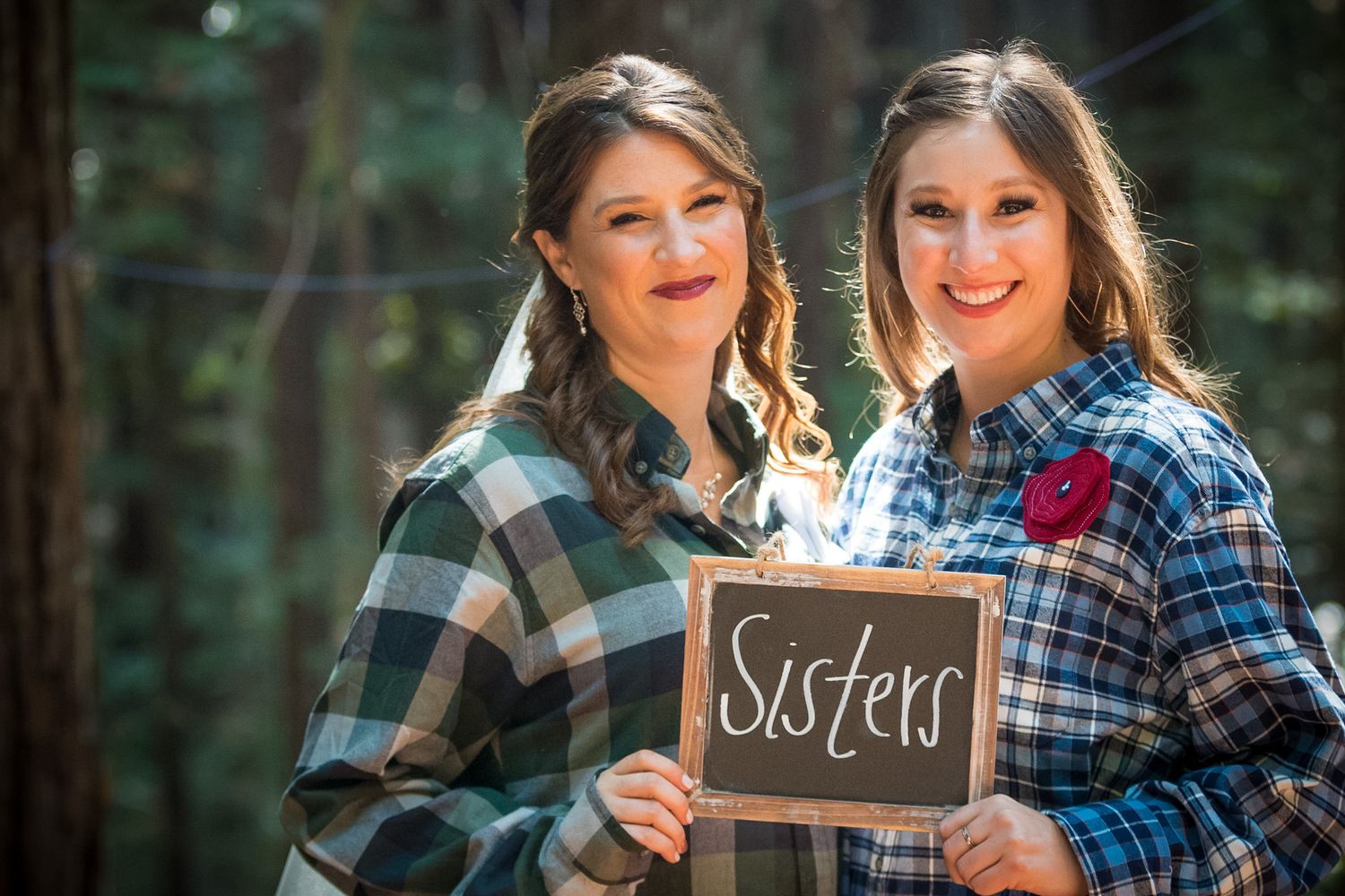 Friends posing with chalkboards in matching plaid shirts in forest setting.
