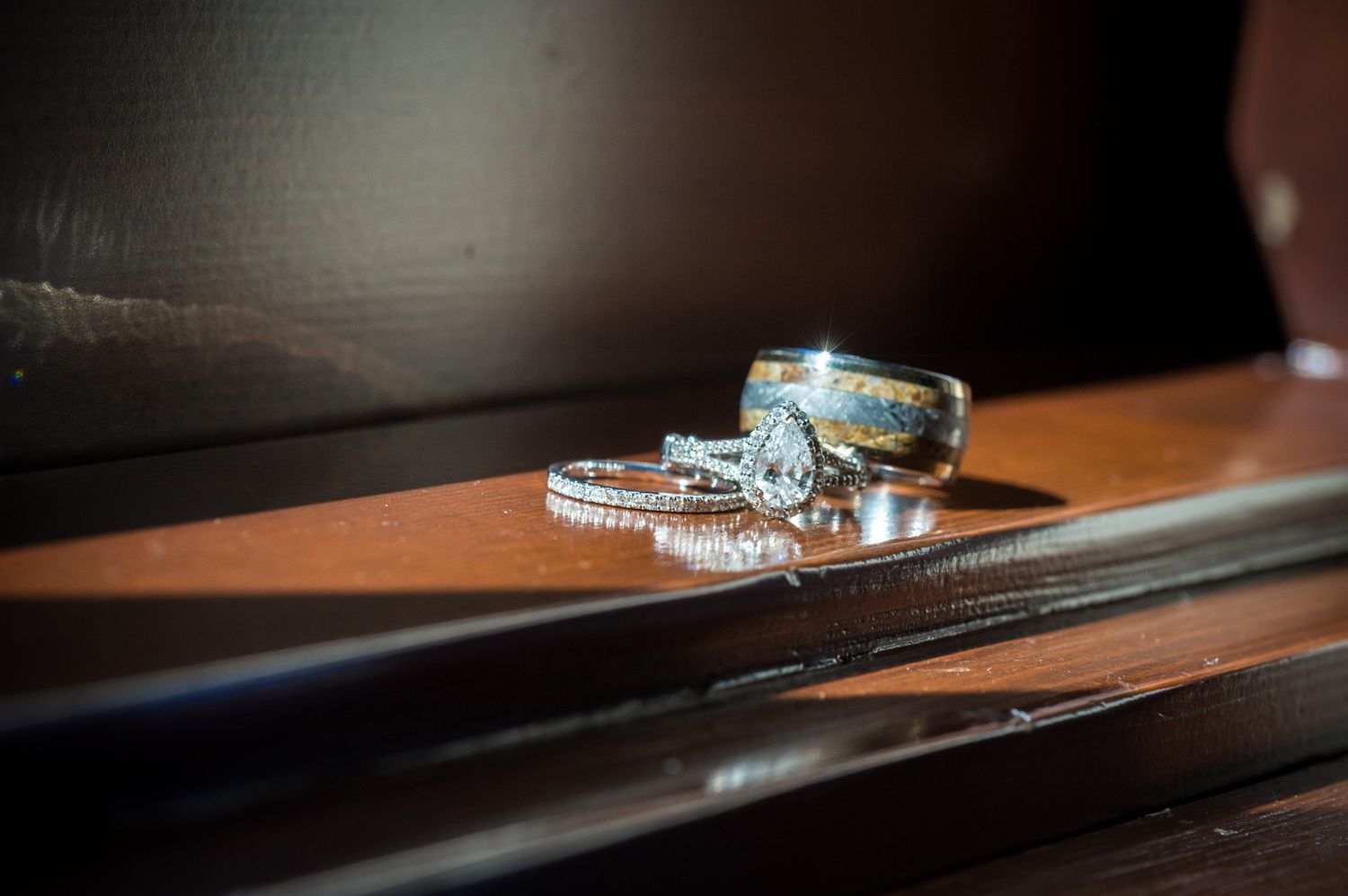 Wedding rings with a turquoise stone engagement ring sit on a wooden ledge in soft natural lighting.