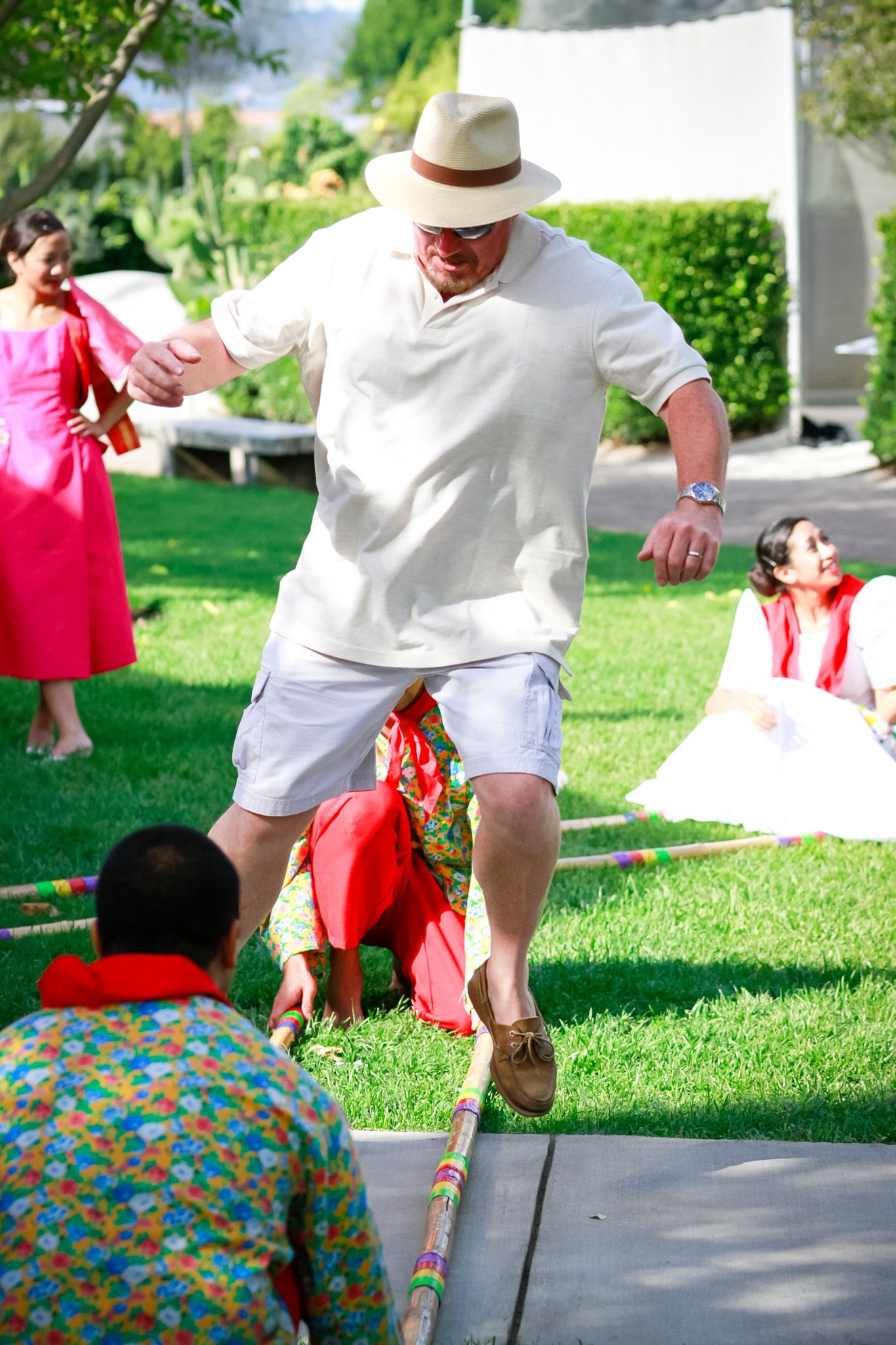 Man in white outfit and hat participating in traditional bamboo stick dance game.