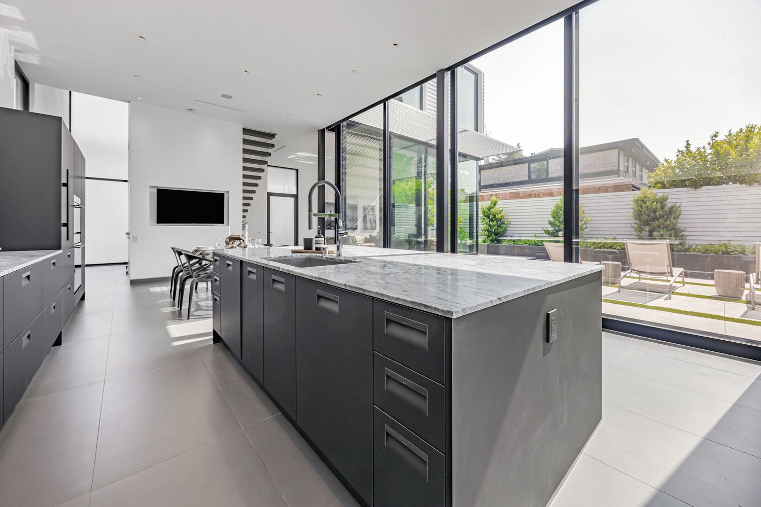 Modern kitchen with black lower cabinets and white countertops extending along a windowed wall.