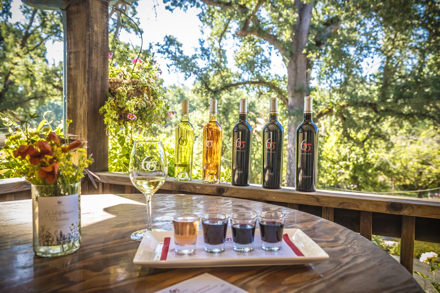 Wine bottles and tasting flight arranged on wooden table with floral centerpiece and natural lighting.