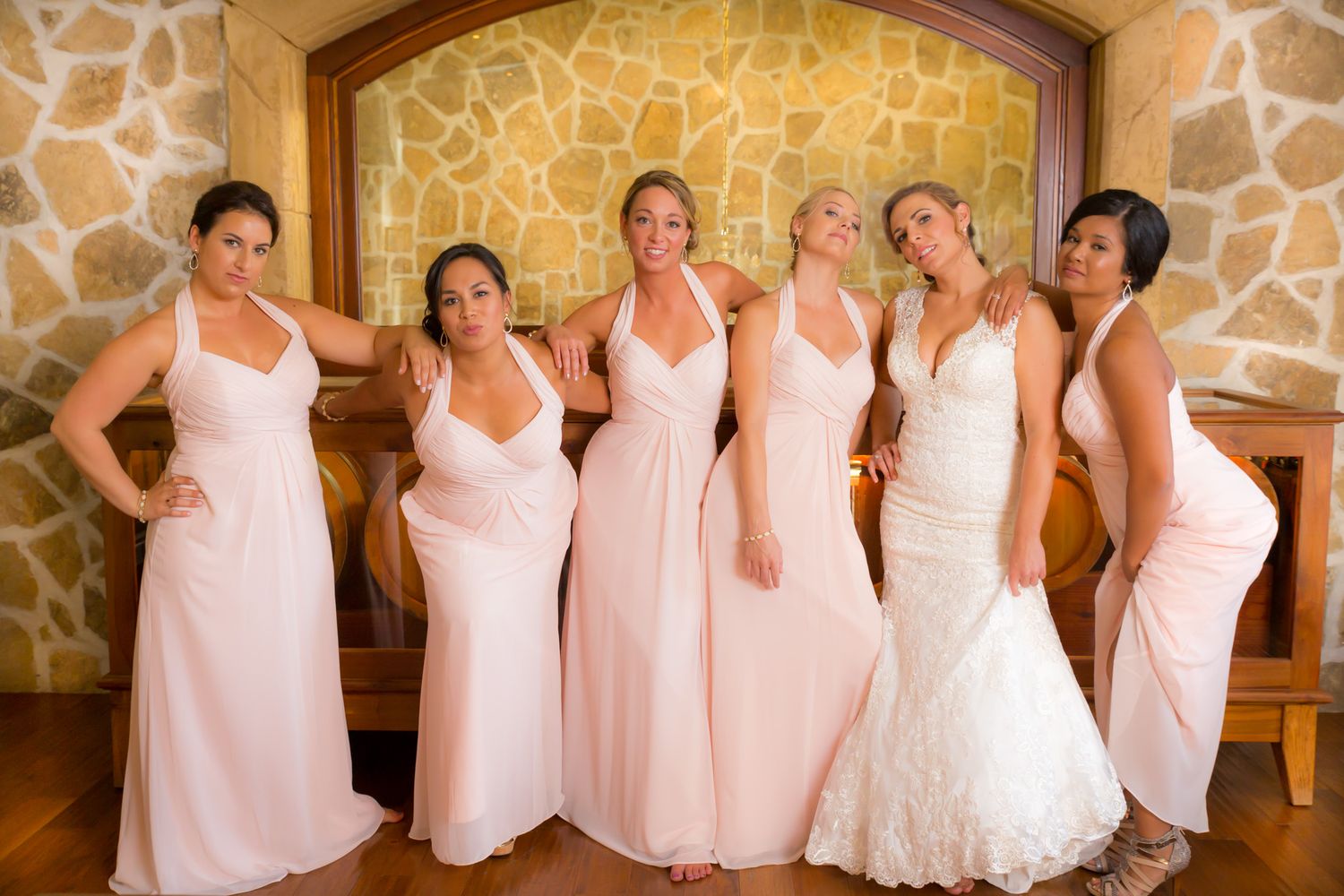 Bridesmaids in elegant white gowns standing together in front of stone archway.
