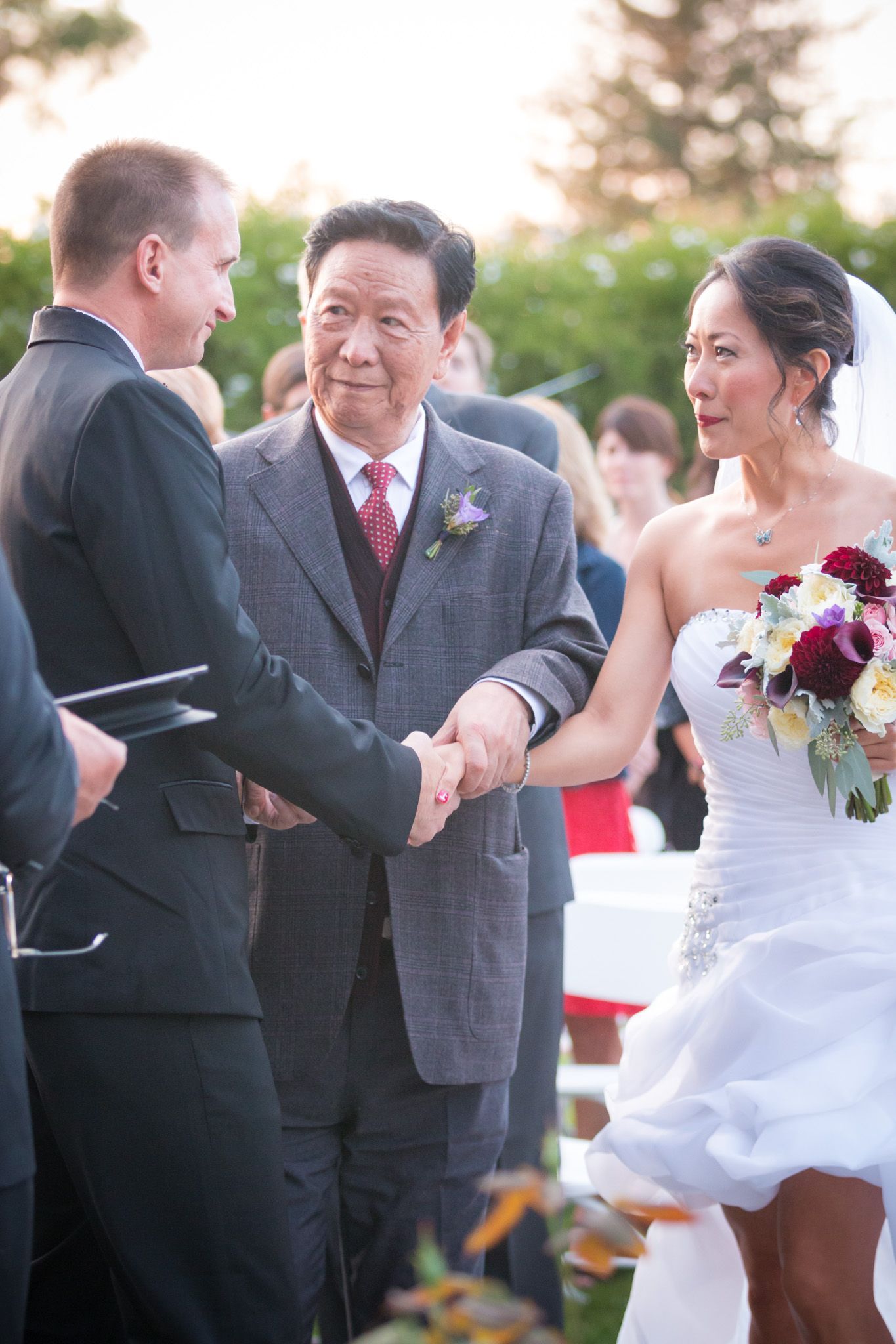 A wedding ceremony takes place outdoors as a couple exchanges vows with an officiant during a beautiful sunset.