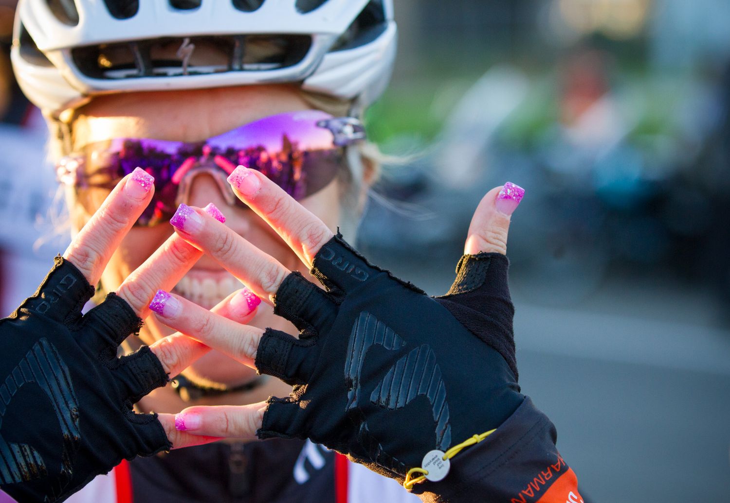 Close-up of cyclist hands wearing fingerless gloves illuminated by pink lighting.