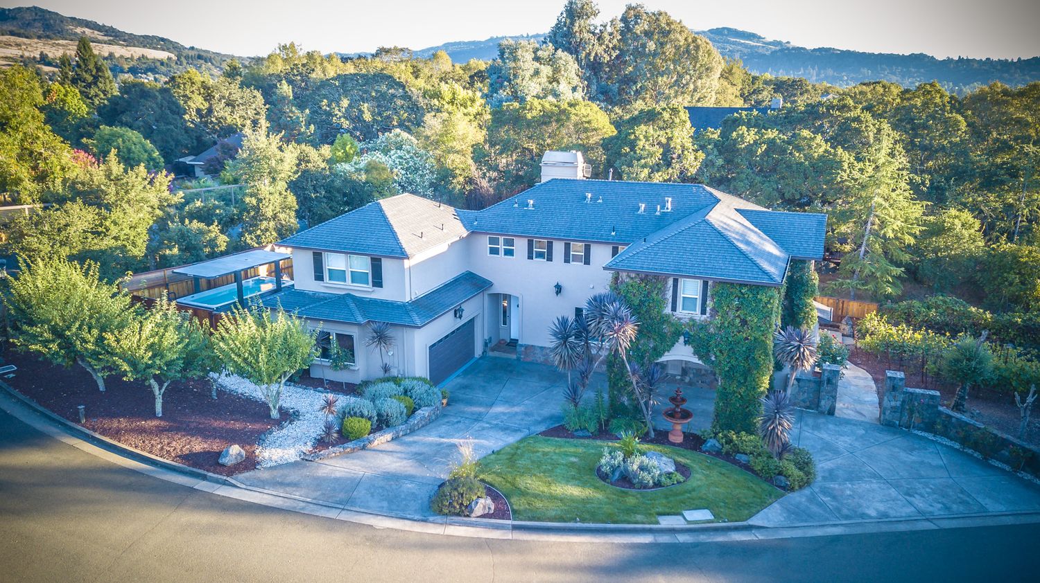 Aerial panorama of suburban houses nestled in green hills under blue sky.