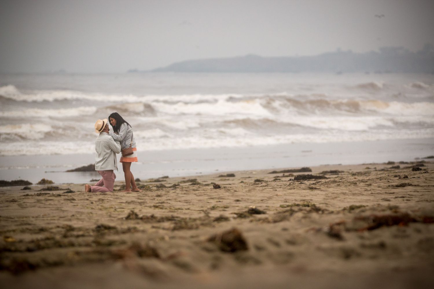 Distant figures on misty beach with dramatic wave backdrop.