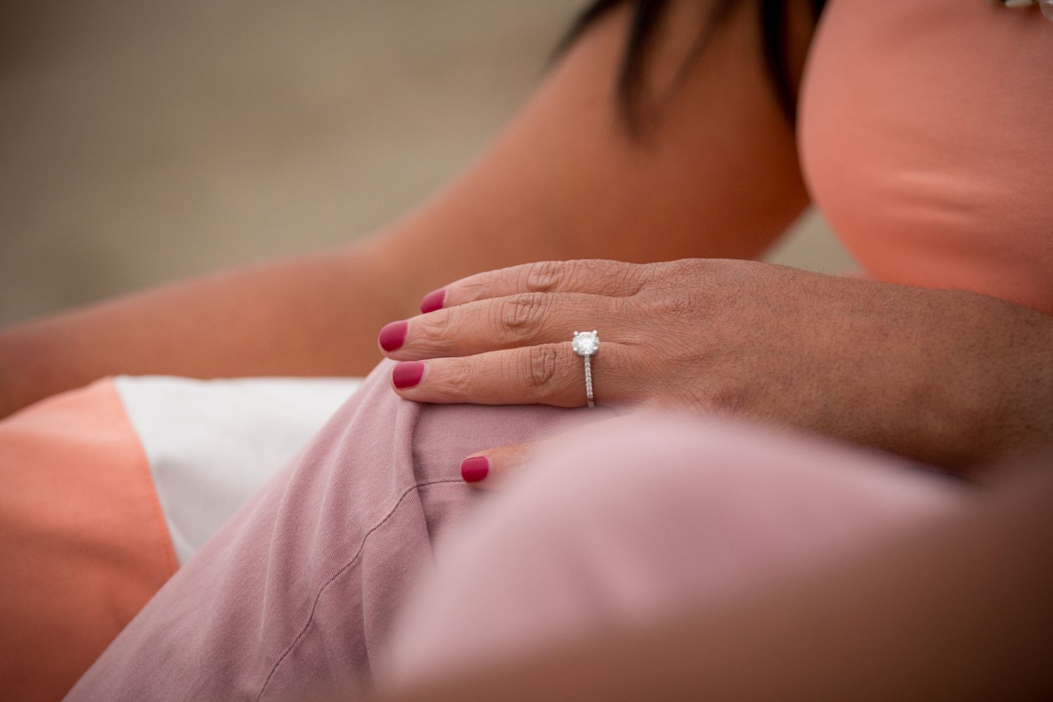 Close-up of hands with engagement ring resting on pink fabric.