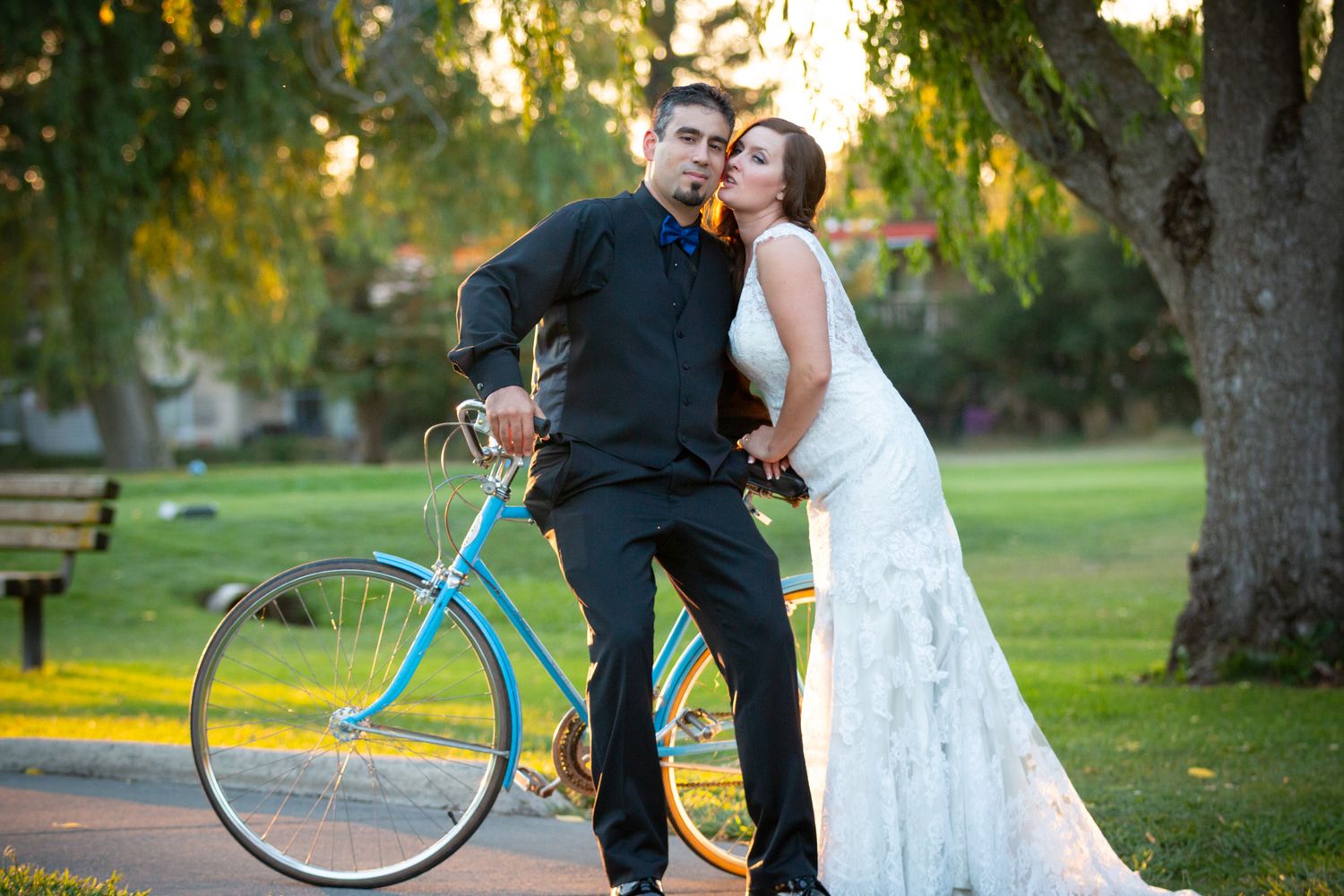A couple poses with a turquoise bicycle in a park during golden hour.