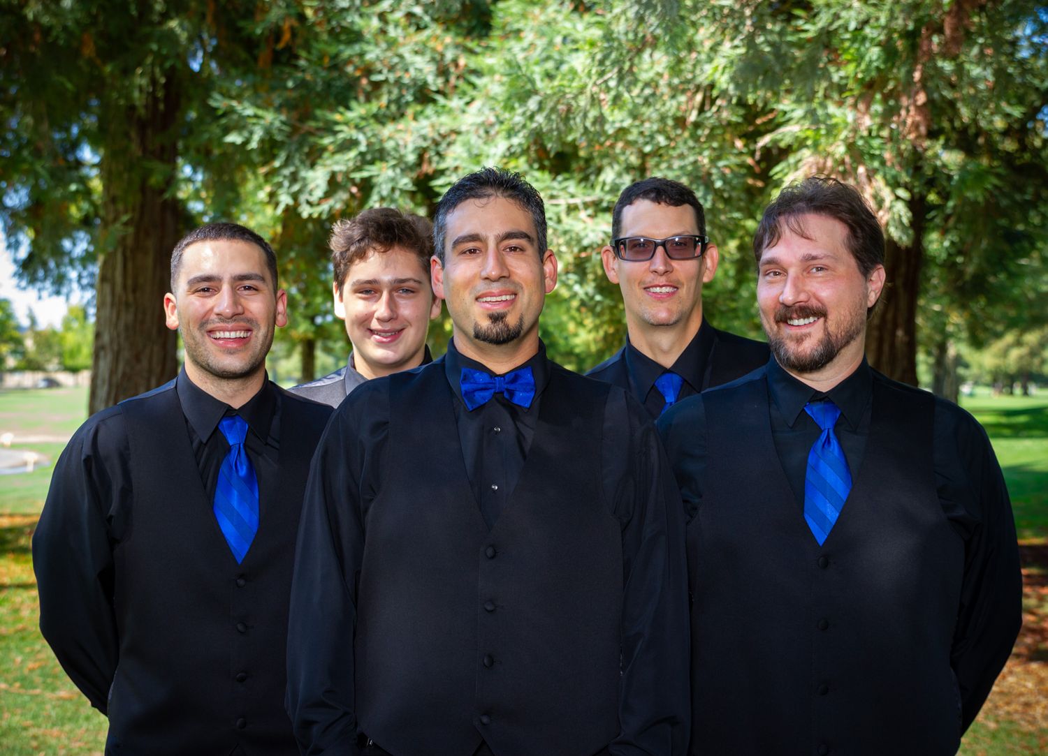 Groomsmen in black suits with royal blue ties pose together outdoors.