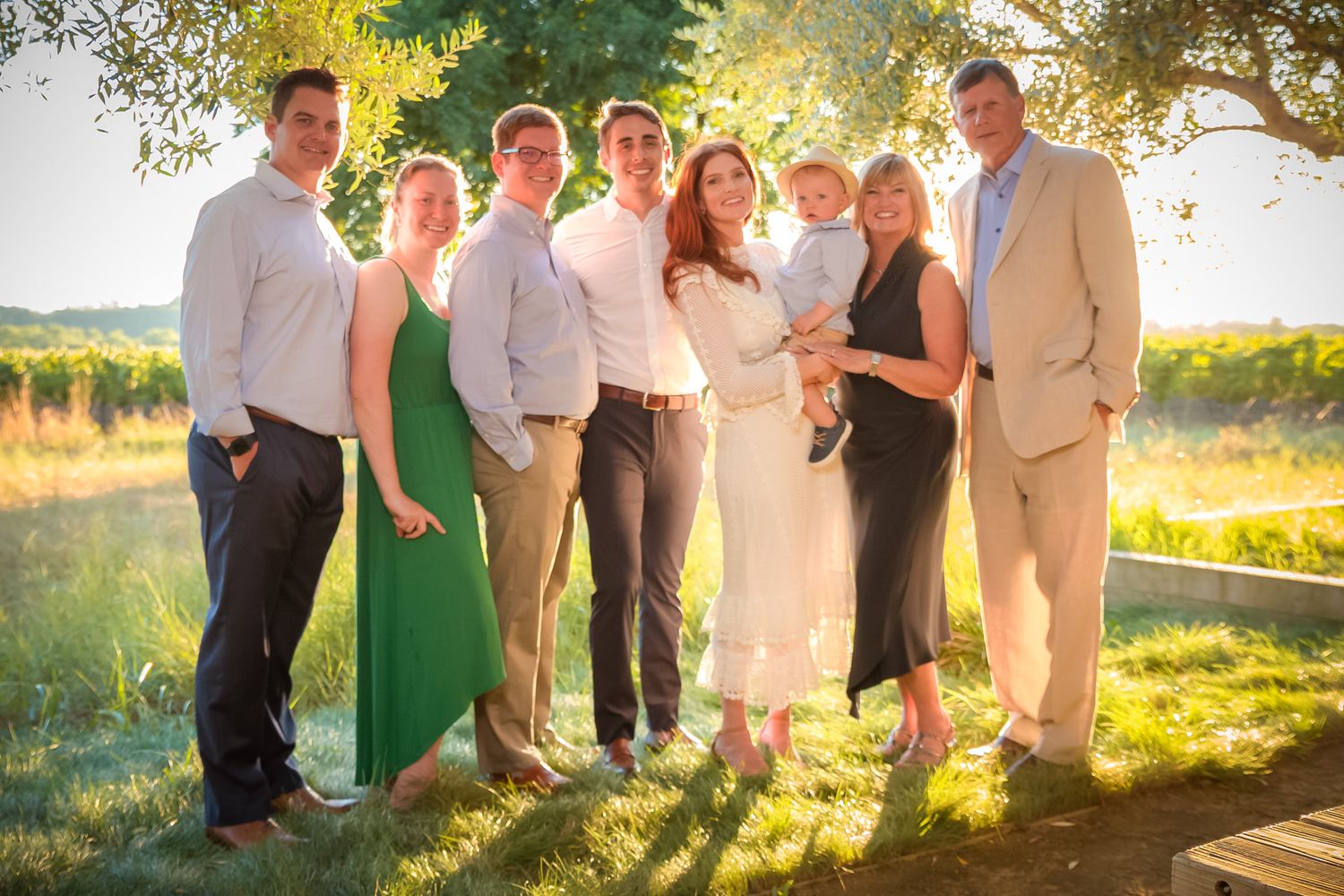 Group photo of elegantly dressed guests at an outdoor event with sunset backdrop.