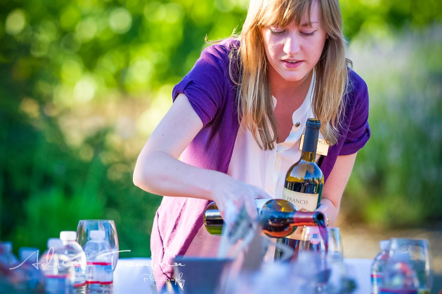 Wine being poured at outdoor tasting event with green natural background.
