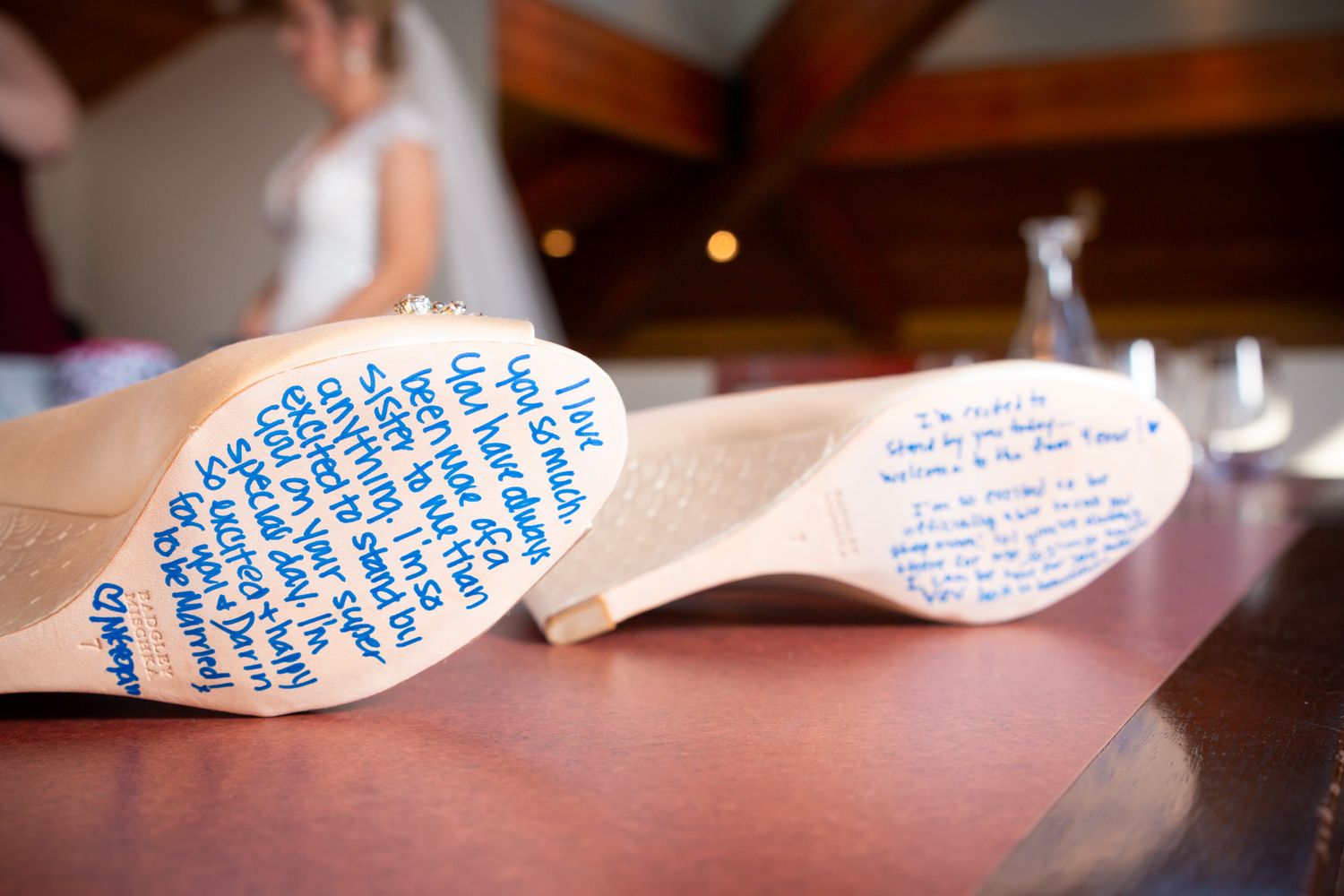 Wedding shoes with handwritten blue messages on the soles sit on a wooden surface.