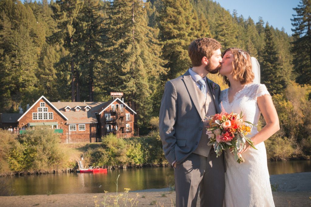 Rustic lakeside wedding portrait with red barn and forest backdrop.