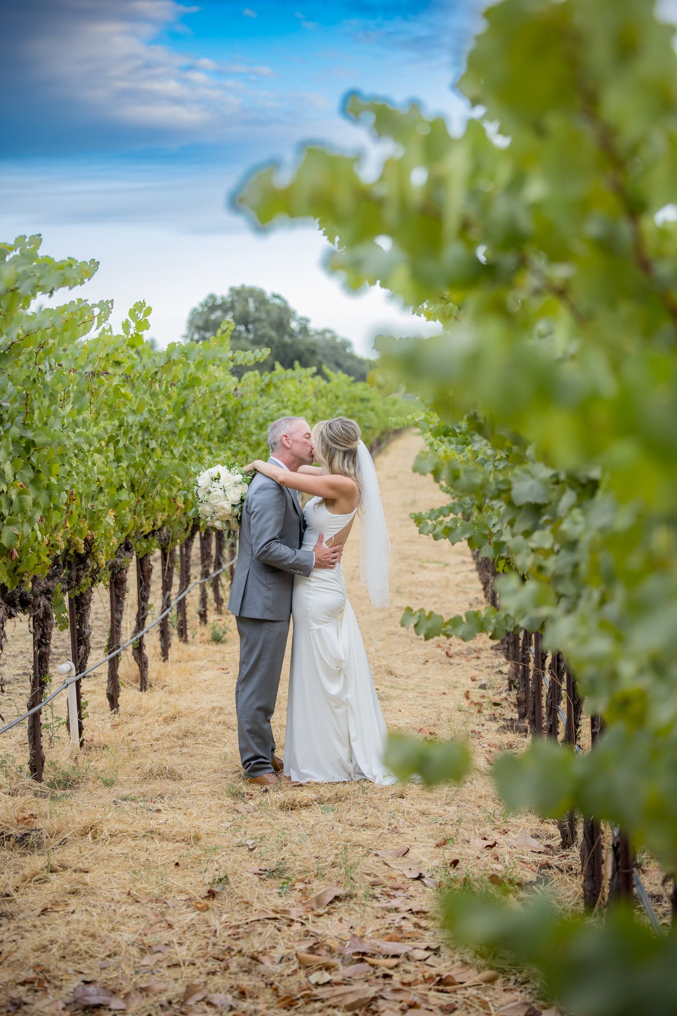 Newlyweds sharing intimate moment in sunlit vineyard.