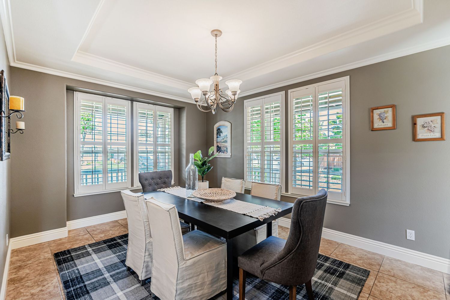 Elegant formal dining room with chandelier, plantation shutters, and plaid area rug under dark wood table.