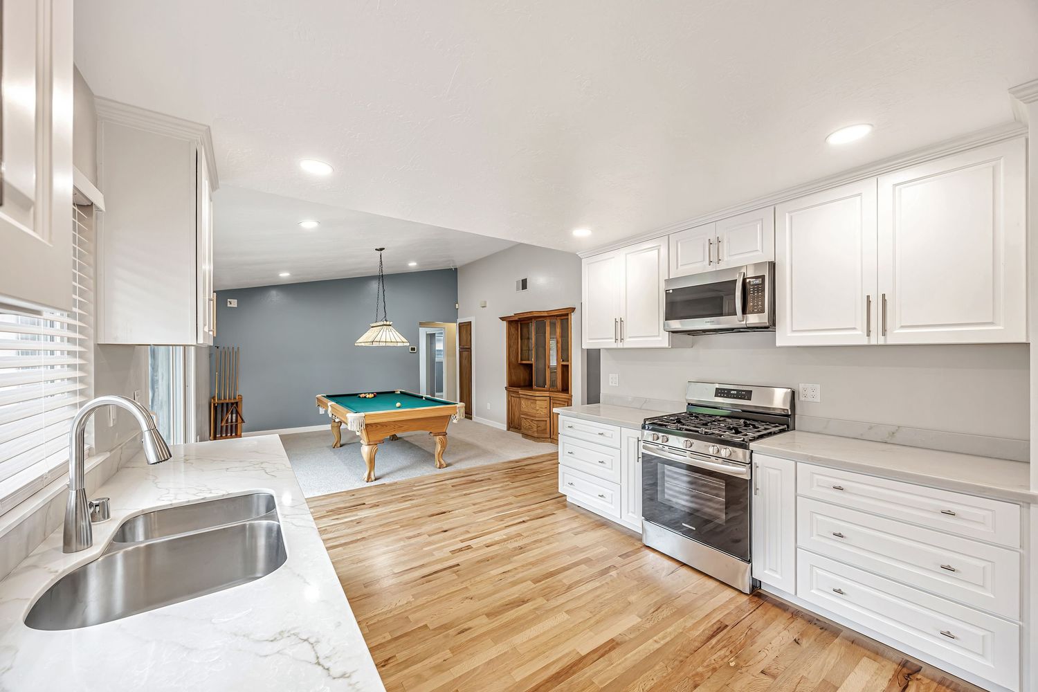 Spacious kitchen with white cabinetry, stainless appliances, and pool table in background.