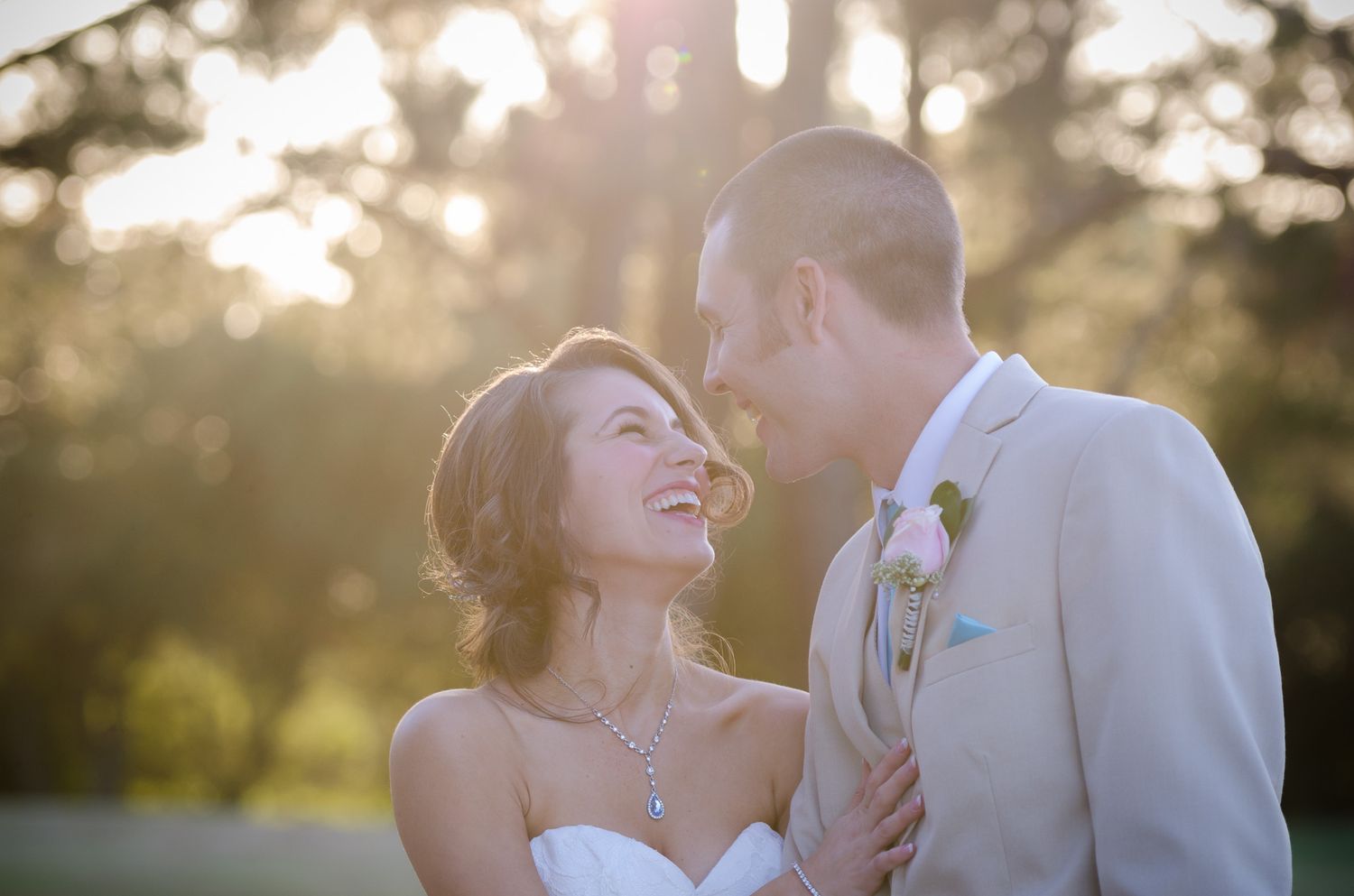 A joyful wedding couple laughs together in golden sunlight during their outdoor photo session.