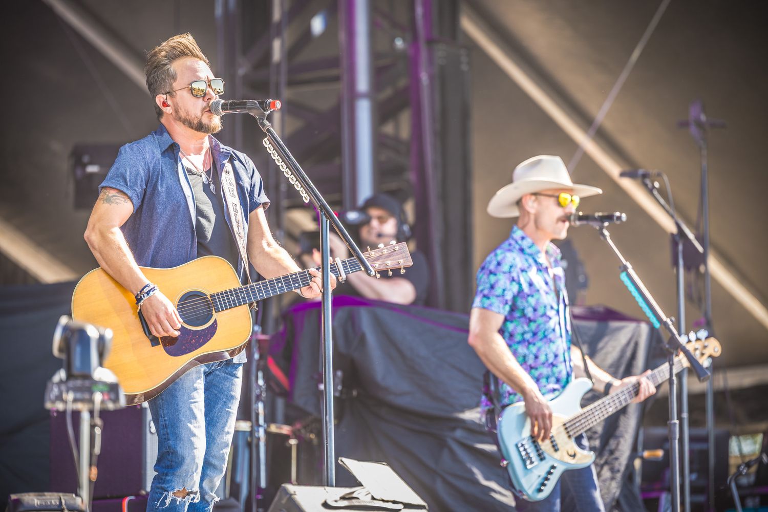 Country musicians perform on outdoor stage with acoustic and electric guitars at summer music festival.