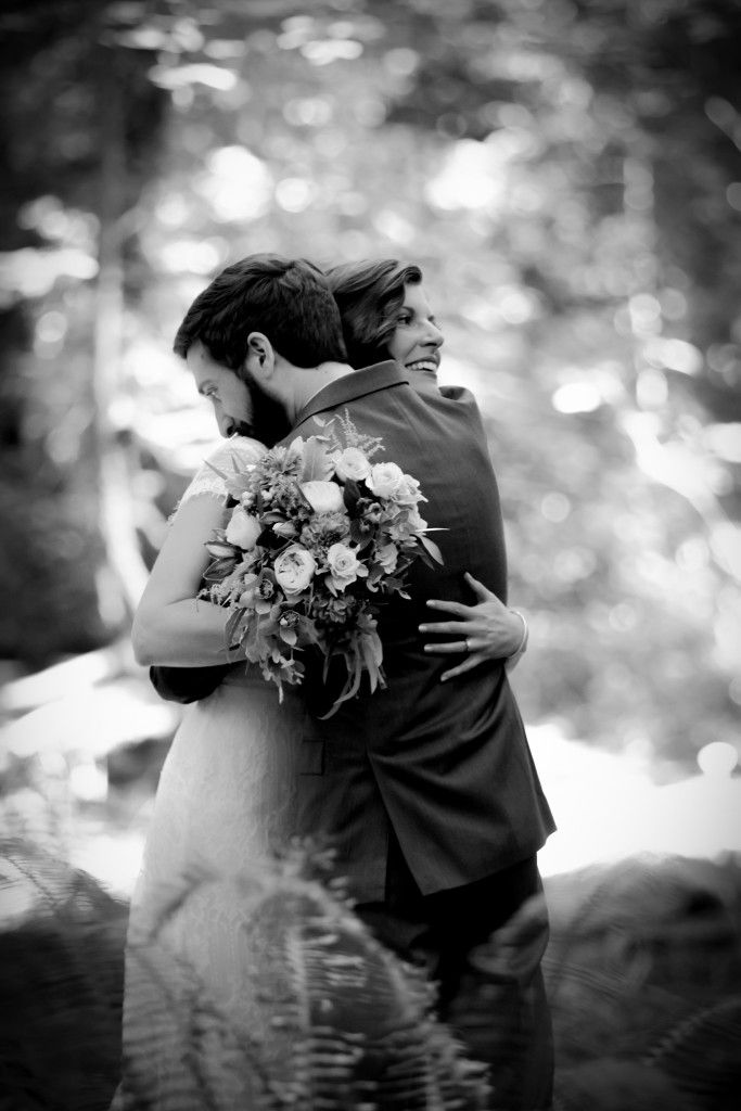 Black and white portrait captures newlyweds embracing in a romantic forest setting.
