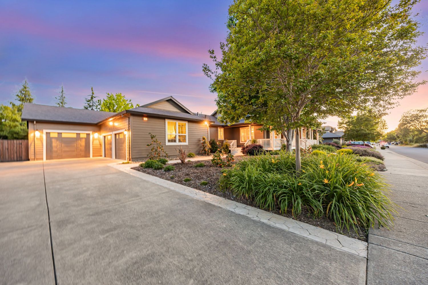 Contemporary home exterior with manicured landscaping and wide concrete driveway at sunset.