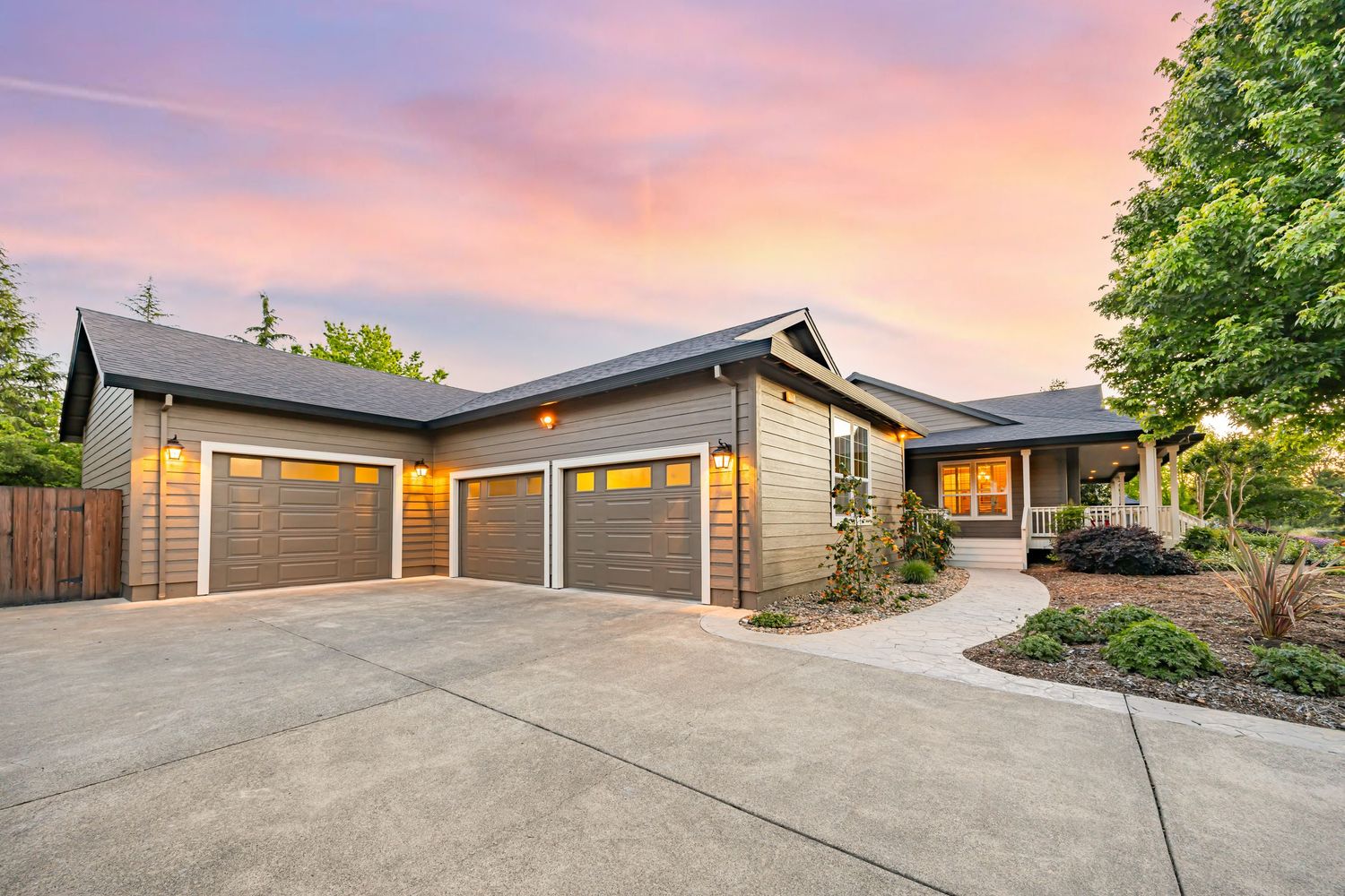 Contemporary home exterior with three-car garage and concrete driveway under pink sunset sky.