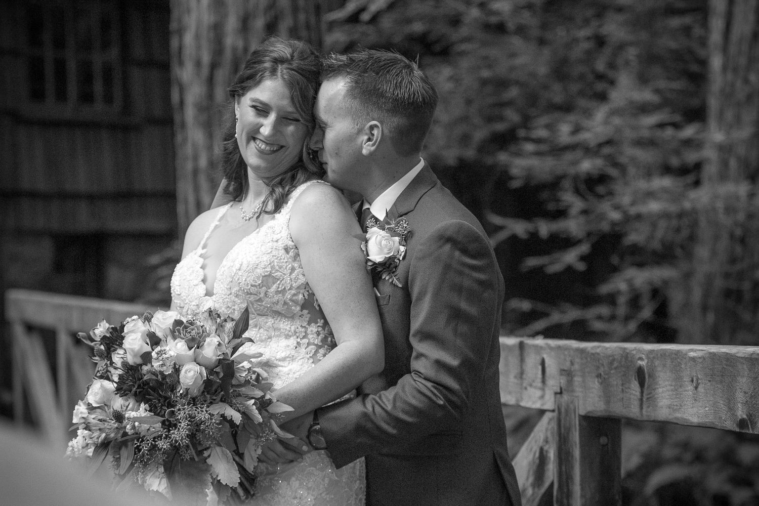 Black and white artistic wedding portrait showing intimate embrace on wooden bridge.