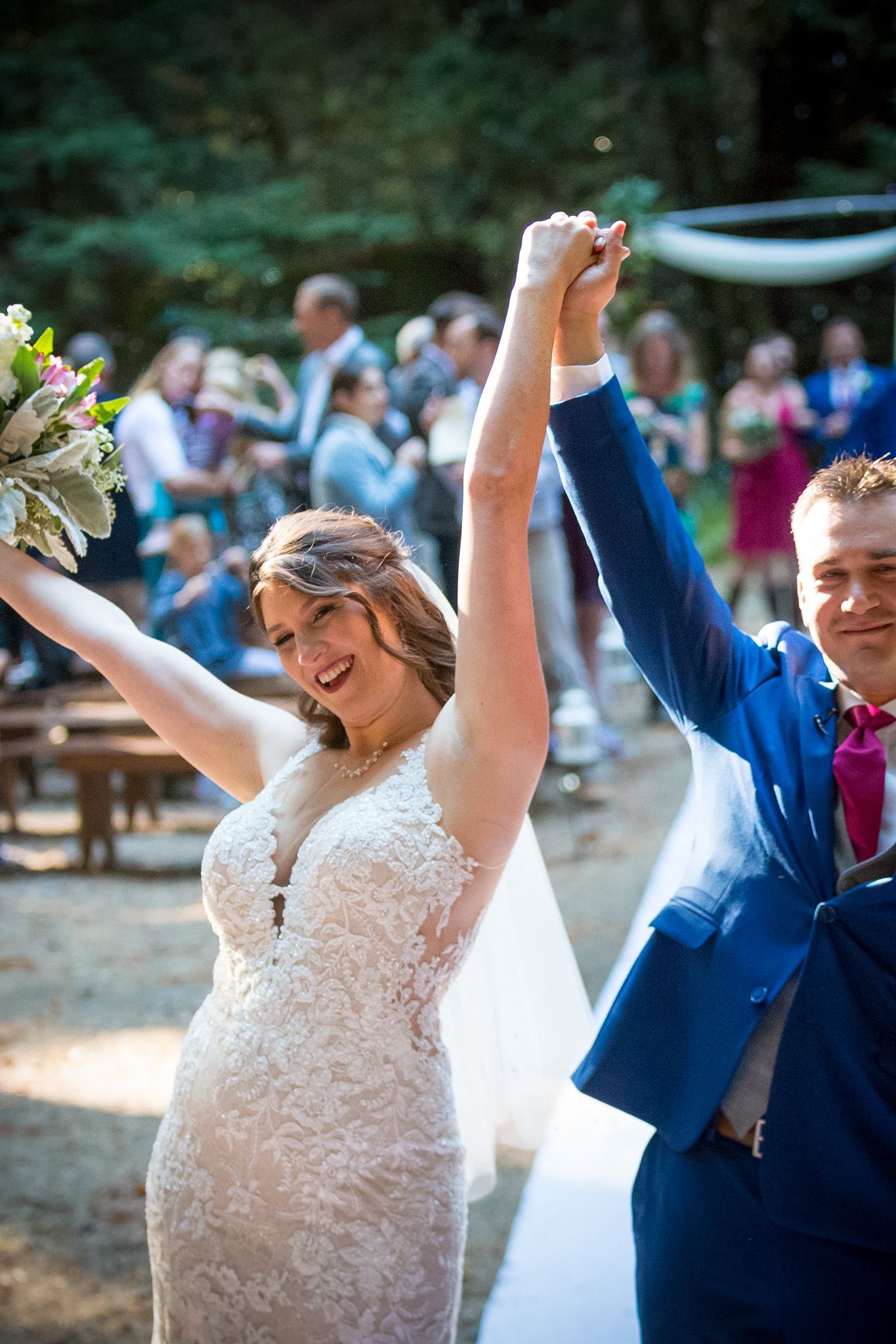 Newlyweds celebrate with raised arms in triumph after their outdoor wedding ceremony.