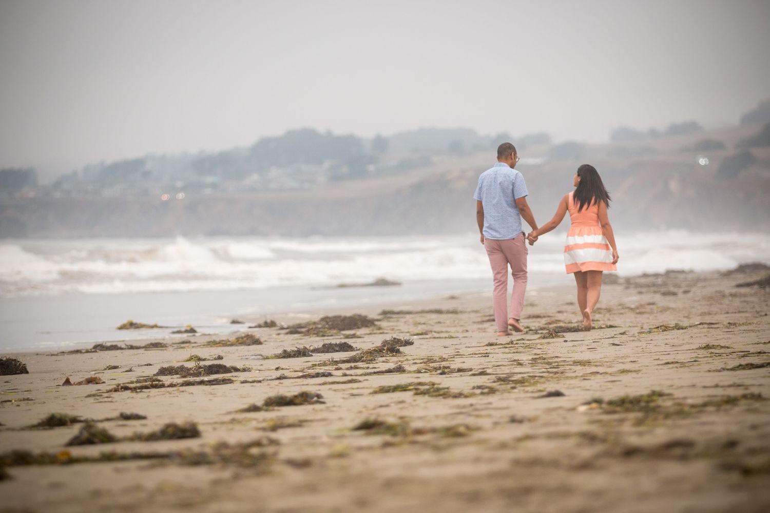 A romantic couple walking together on a sandy beach with waves in the background.