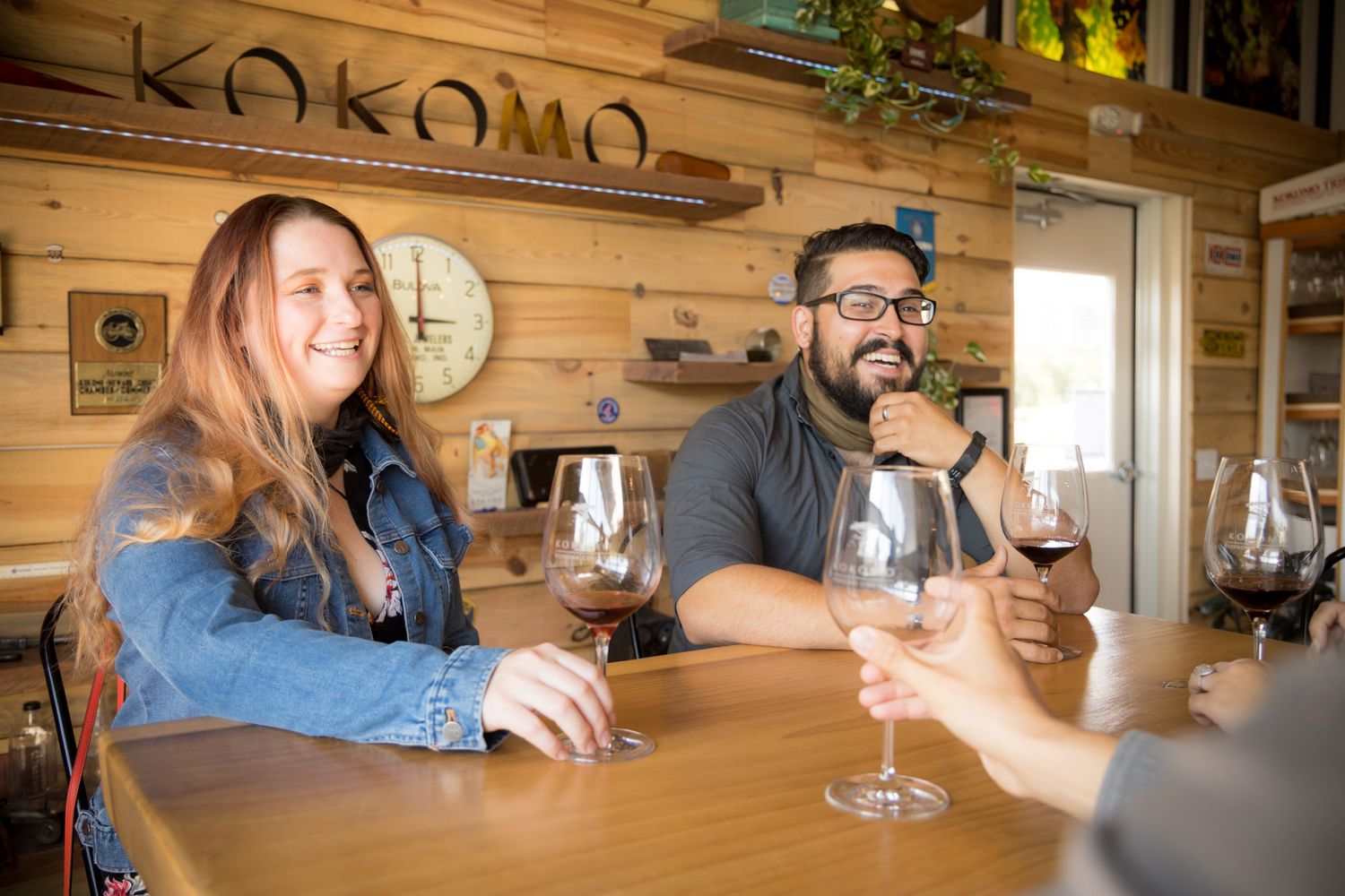 Wine tasting experience at rustic wooden bar with Kokomo signage.