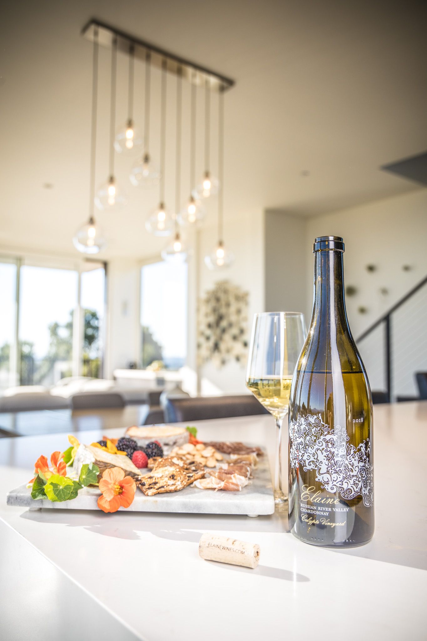 Wine bottle and charcuterie board displayed under pendant lighting in modern setting.