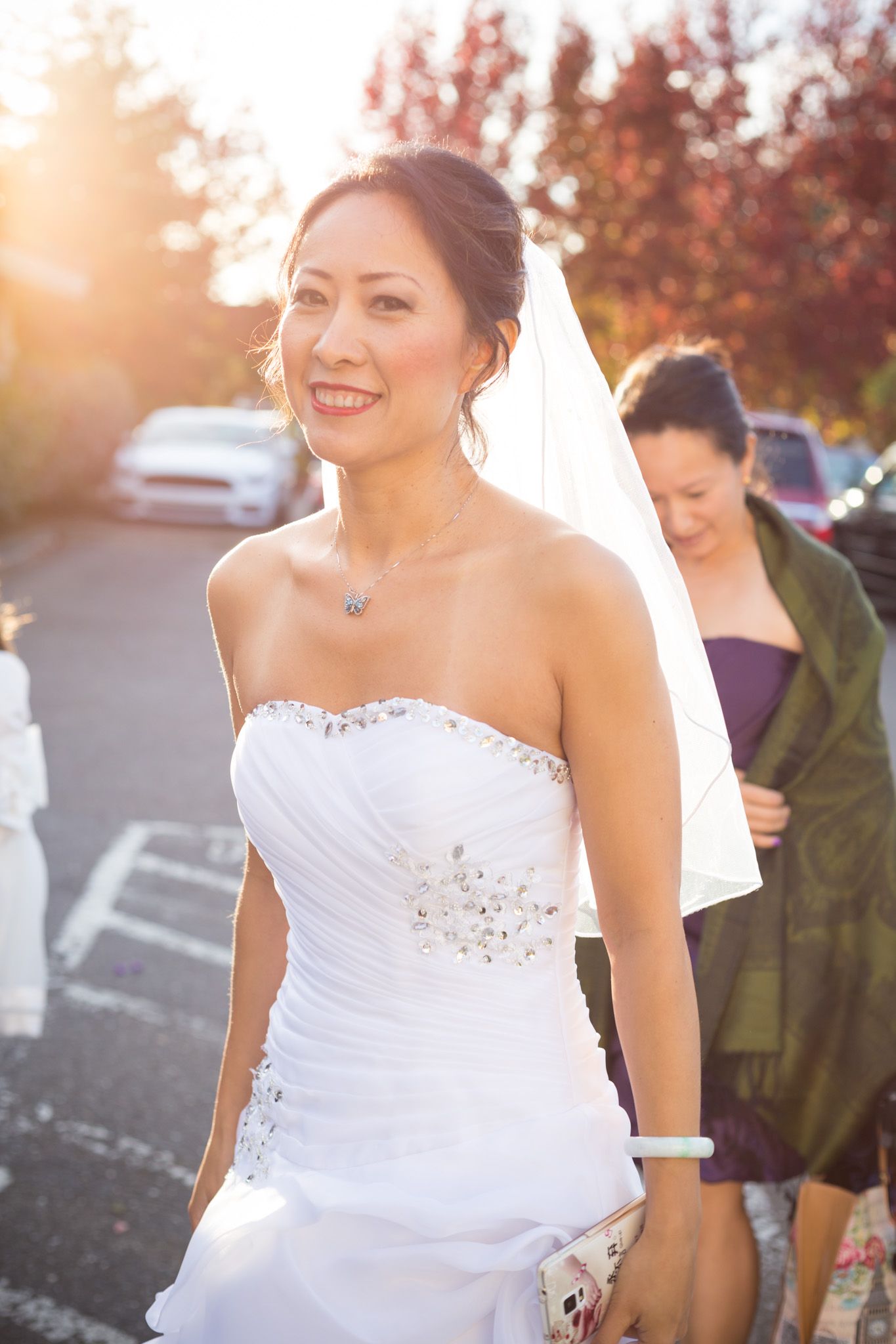 A bride in a stunning white strapless wedding dress with beaded embellishments poses in warm sunset lighting.