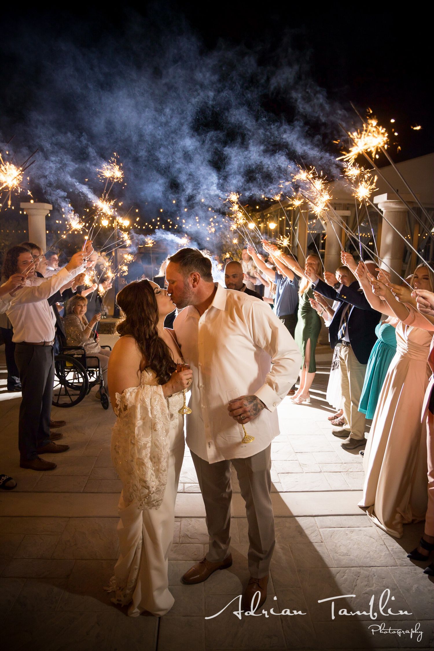 A romantic sparkler send-off illuminates a wedding couple's exit through a tunnel of guests.