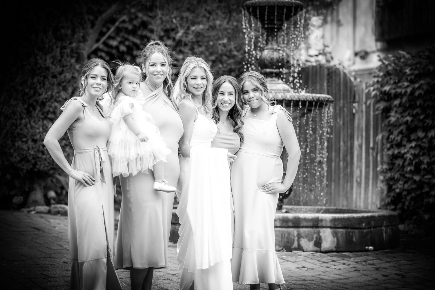 Black and white wedding photo of bridal party posing by fountain.