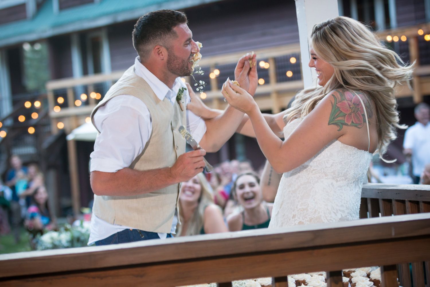 A couple shares a playful dance moment on a wooden deck with twinkling lights in the background.