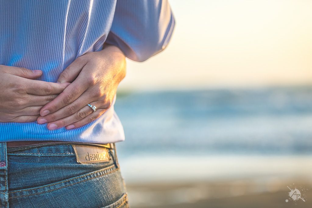 Person with hands on lower back experiencing pain at beach during sunset.